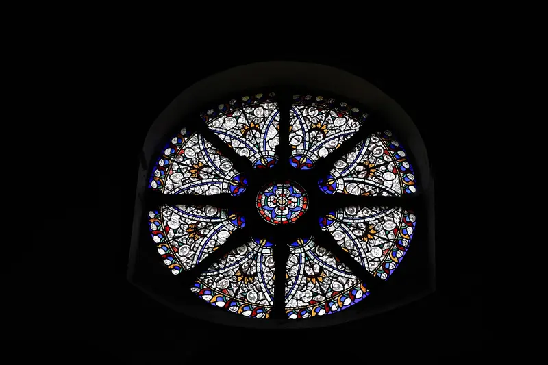 A round wheel window of blue and gold Victorian stained glass glowing against dark stone