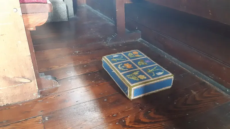 An embroidered church kneeler in blue and gold lying on a polished wooden floor in a shaft of light