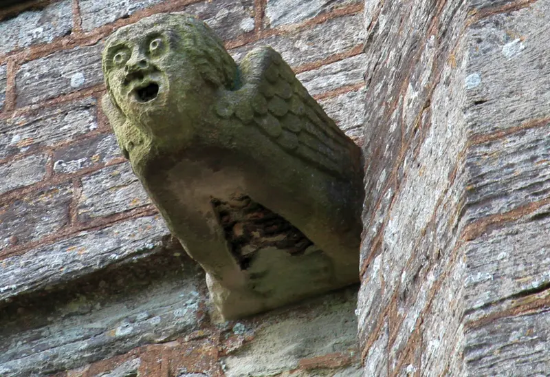 A carved stone gargoyle with a surprised open-mouthed face on a church wall